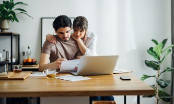 Un couple étudie un document devant un ordinateur, à son domicile. 