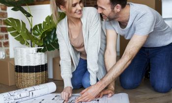Un couple agenouillé sur le sol échange devant le plan de sa future maison