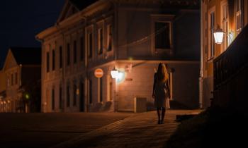 Une femme élégante marche seule sur le trottoir dans une rue sombre
