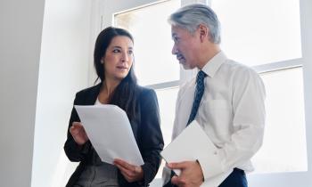 Un homme et une femme adossés contre une fenêtre échangent à propos d'un document