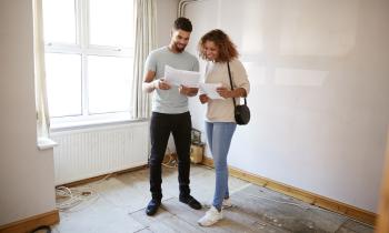 Un couple étudie des documents dans une pièce de son logement nécessitant des travaux de rénovation