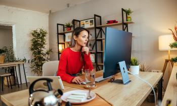 Une femme, installée à un bureau, consulte des documents sur son ordinateur personnel, dans son salon