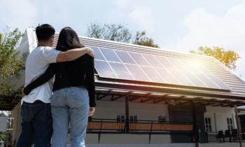 Couple enlacé, debout près de sa maison sur laquelle ont été installés des panneaux photovoltaïques