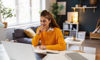 Une femme souriante télétravaille sur une table, dans son salon 