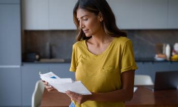 Une femme, debout dans sa cuisine, découvre les documents qu'elle a reçus par courrier