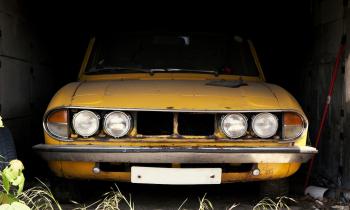 Une voiture de collection jaune en mauvais état est en stationnement dans un garage