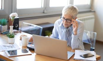 Une femme aux cheveux blancs très courts se charge de dossiers administratifs sur son pc portable