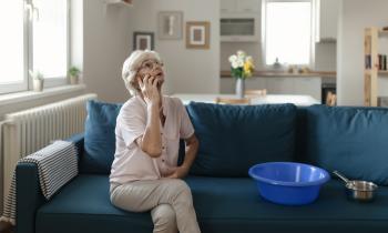 Une femme d'âge mûr, assise sur son canapé, est en communication téléphonique au sujet d'un dégât des eaux dans son salon
