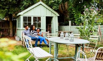 Une famille profite de son espace jardin, installée sur un banc devant un bel abri de jardin