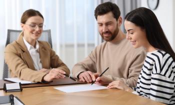 Un jeune couple signe les documents relatifs à l'achat de son nouveau logement chez le notaire