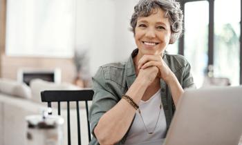 Une femme aux cheveux courts gris, assise devant son pc portable, affiche un sourire satisfait