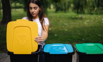 Une jeune femme aux cheveux longs  jette un emballage dans le bac de tri jaune