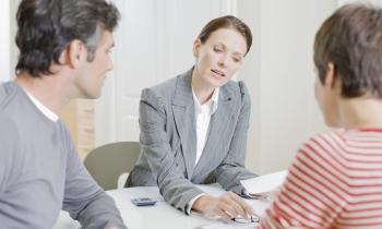 Une femme donne des explications à un couple de clients sur des documents au format papier