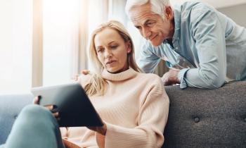 Une femme assise sur un canapé consulte des informations sur une tablette, son mari se tient penché au-dessus d'elle