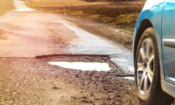 Une voiture emprunte une route endommagée, présentant plusieurs nids-de-poule remplis d'eau
