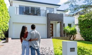 Un jeune couple enlacé admire la maison neuve qu'il vient d'acquérir
