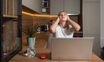 Une jeune femme travaillant sur son pc portable se bouche les oreilles en regardant le plafond de son appartement