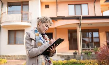 Une femme agent immobilier prend des notes sur une maison, dans la rue, en vue de son évaluation immobilière