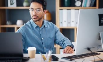 Un homme brun portant des lunettes fait des recherches sur son ordinateur de bureau