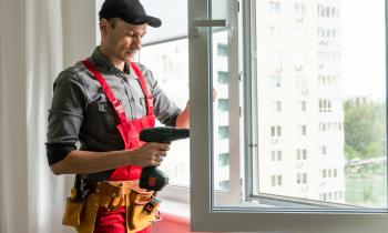 Un artisan, en salopette et casquette, installe un nouveau vitrage sur la fenêtre d'un logement
