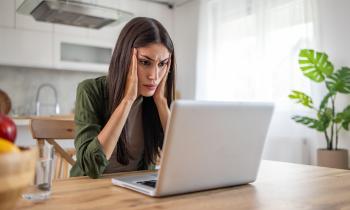 Une femme brune aux cheveux longs se tient la tête dans ses mains devant son pc portable, soucieuse