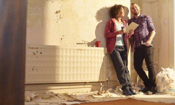 Un couple adossé contre un mur regarde avec satisfaction l'appartement qu'il est en train de rénover
