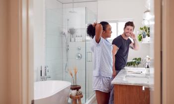 Un homme et une femme en pyjama se sourient devant le miroir de leur magnifique salle de bain