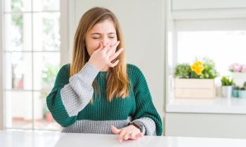 Une jeune femme se bouche le nez, en grimaçant, gênée par une mauvaise odeur