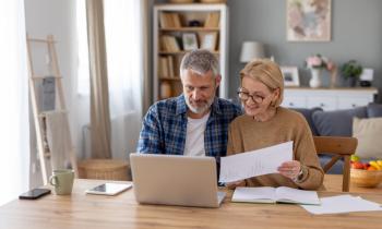 Un couple d'âge mûr réalise une étude sur son pc portable, dans son salon