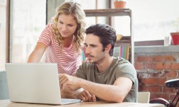 Un jeune couple étudie avec attention des dossiers sur un ordinateur portable