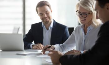 Une femme blonde signe un contrat chez le notaire, avec un grand sourire