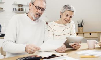 Un couple d'âge mûr assis à une table réalise une étude, à l'aide d'une tablette et d'une calculatrice