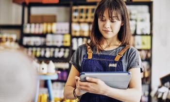 Une jeune entrepreneure portant une salopette en jean travaille à l’aide de sa tablette numérique dans son épicerie fine