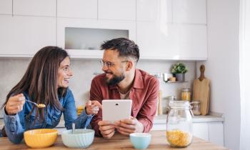 Couple déjeune en lisant leur sur leur tablette la mine réjouie
