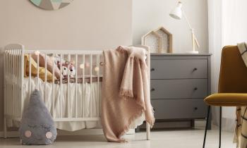 Une chambre d'enfant dans les tons roses avec un lit de bébé et une commode grise