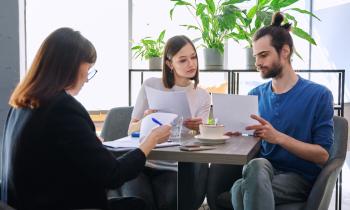 Un jeune couple étudie des documents au cours d'un rendez-vous avec une professionnelle de l'immobilier