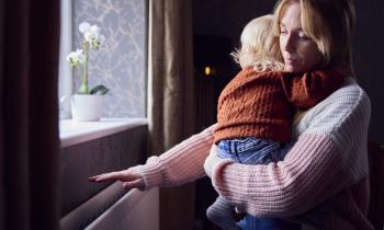 Une maman tenant son bébé dans les bras passe la main au-dessus du chauffage mural pour voir s'il fonctionne