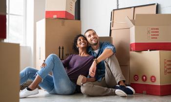 Un jeune couple est assis par terre enlacé, en admirant son nouveau logement rempli de cartons de déménagement