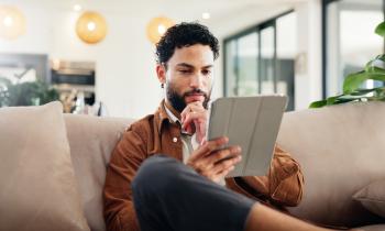 Un homme assis sur son canapé consulte des informations sur une tablette