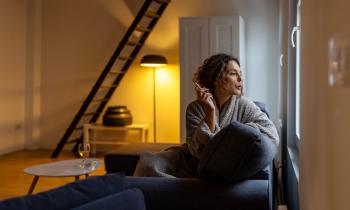 Une femme, assise sur son canapé, regarde par la fenêtre en fumant une cigarette
