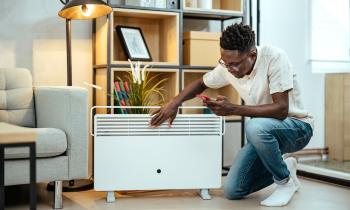 Un homme règle la consommation de son radiateur électrique à l'aide de son smartphone, agenouillé devant l'appareil dans son salon