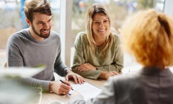 Un couple souriant valide les conditions d'un accord avec sa conseillère bancaire lors d'un rendez-vous