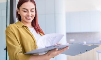Une jeune femme aux cheveux roux sourit, tout en feuilletant un dossier au format papier