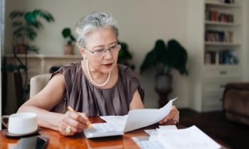 Une femme d'âge mûr vérifie ses factures sur sa table de salon, à l'aide de sa calculatrice