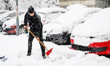Un homme déneige le parking d'une copropriété à l'aide d'une pelle