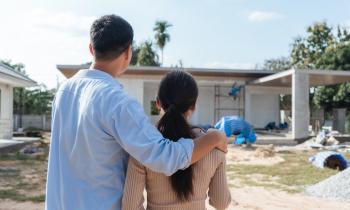 Un jeune couple s’enlace tout en regardant l’avancement de sa maison sur le chantier