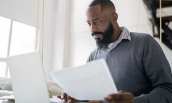Un homme étudie des documents sur son pc portable, un document à la main