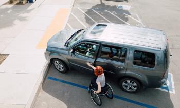 Une femme se déplaçant en fauteuil roulant ouvre la portière avant de son véhicule garé sur une place handicapé