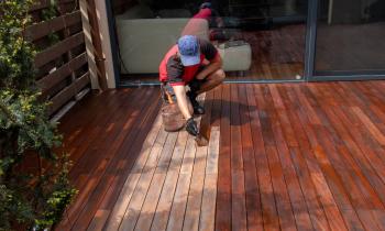 Un homme passe une couche de produit au pinceau sur une terrasse en bois pour la protéger et lui redonner de l'éclat