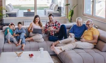 Une famille réunie sur le grand canapé d'angle gris qui consulte : ordinateurs et telephones...
